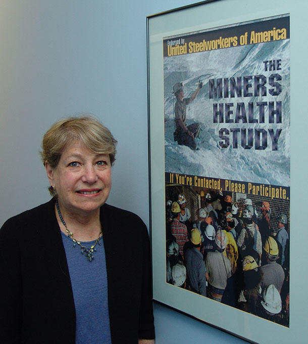 Debra Silverman standing next to a poster that reads "The Miners Health Study". The poster depicts various images of workers in hard hats.