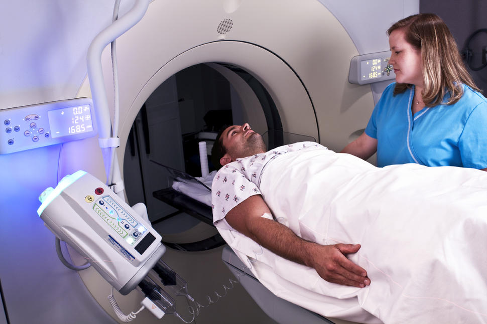 A nurse guides a patient, who is laying down, into a CT machine.