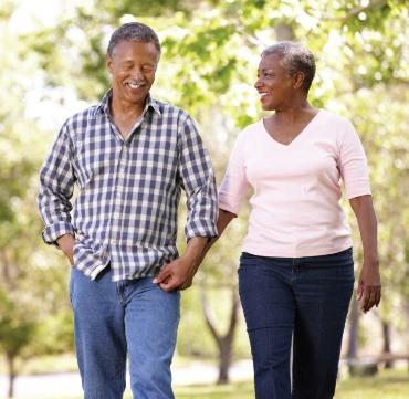 A man and woman, both mature African Americans who are dressed in casual clothing and smiling, walk outside. 