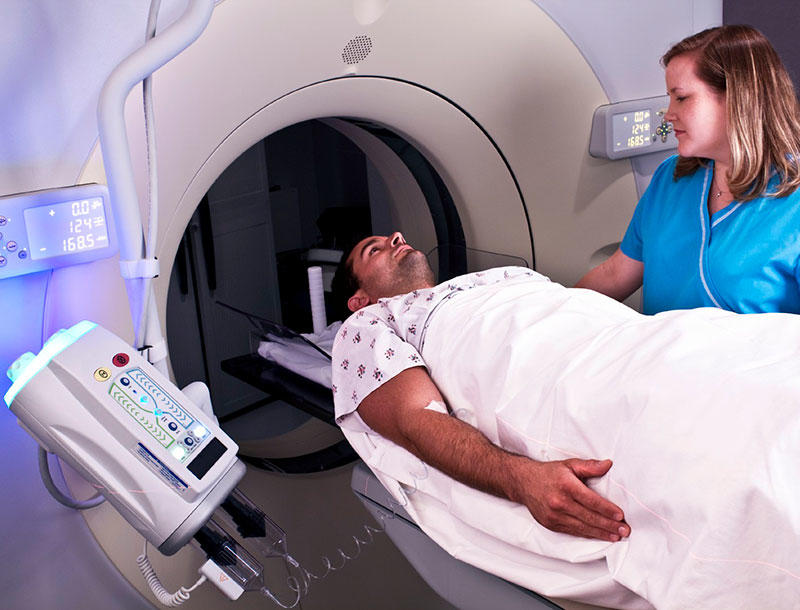 A nurse guides a patient, who is laying down, into a CT machine.