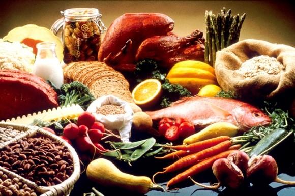 A display of healthy foods on a table. Foods include beans, grains, cauliflour, cantelope, pasta, bread, orange, turkey, salmon, carrots, turnips, zucchini, snowpeas, string beans, radishes, asparagus, summer squash, lean beef, tomatoes, and potatoes.