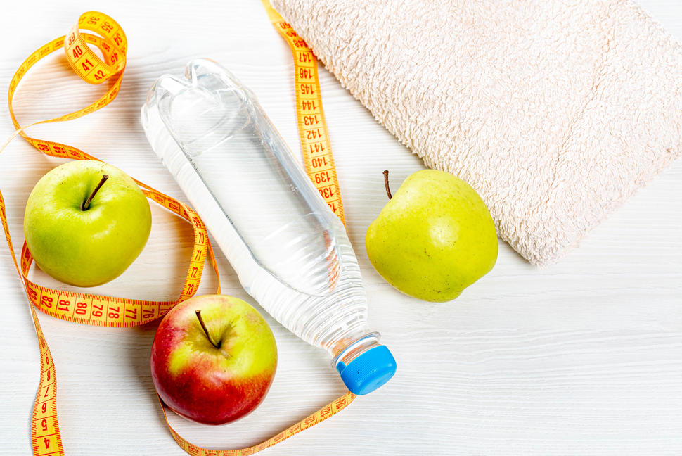 Water bottle, apples, measuring tape and towel on white wooden background. Top view
