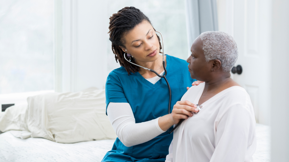 A healthcare provider checks the heart rate of a patient with a stethoscope. They are both Black women. 