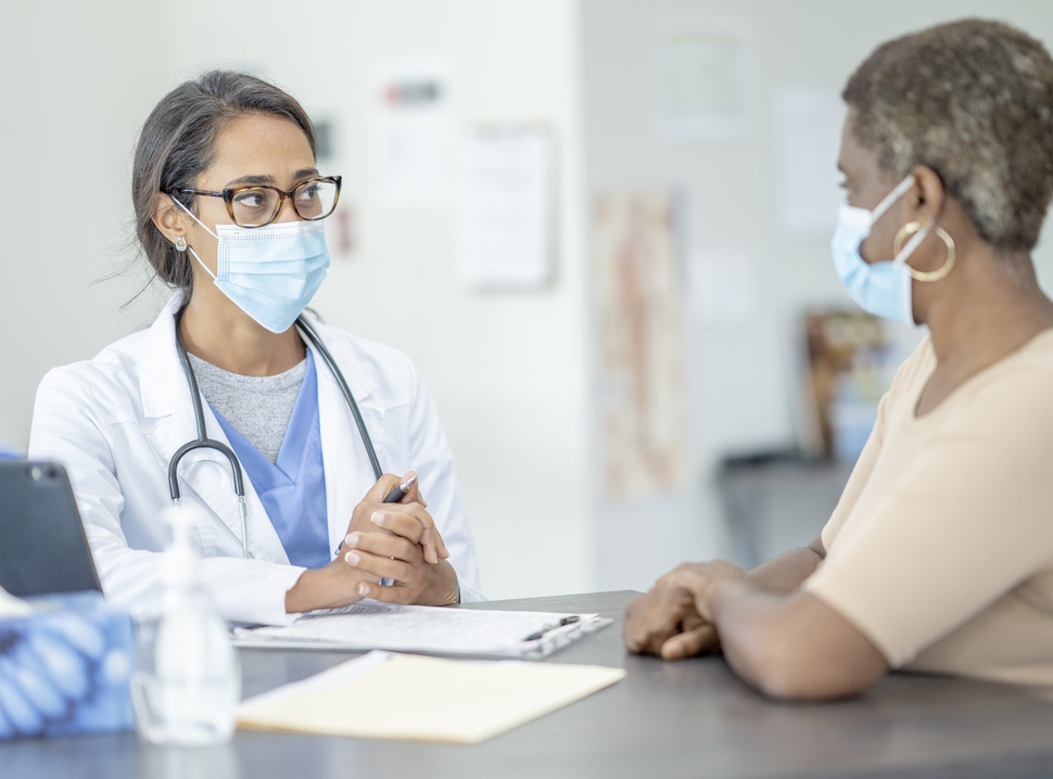 Female doctor wearing a mask speaking with a female patient wearing a mask