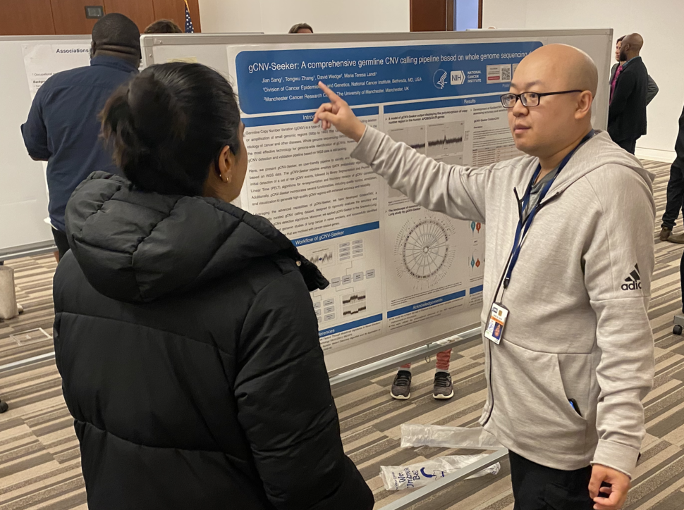 Jian Sang points to his poster as he explains his research to another person. 