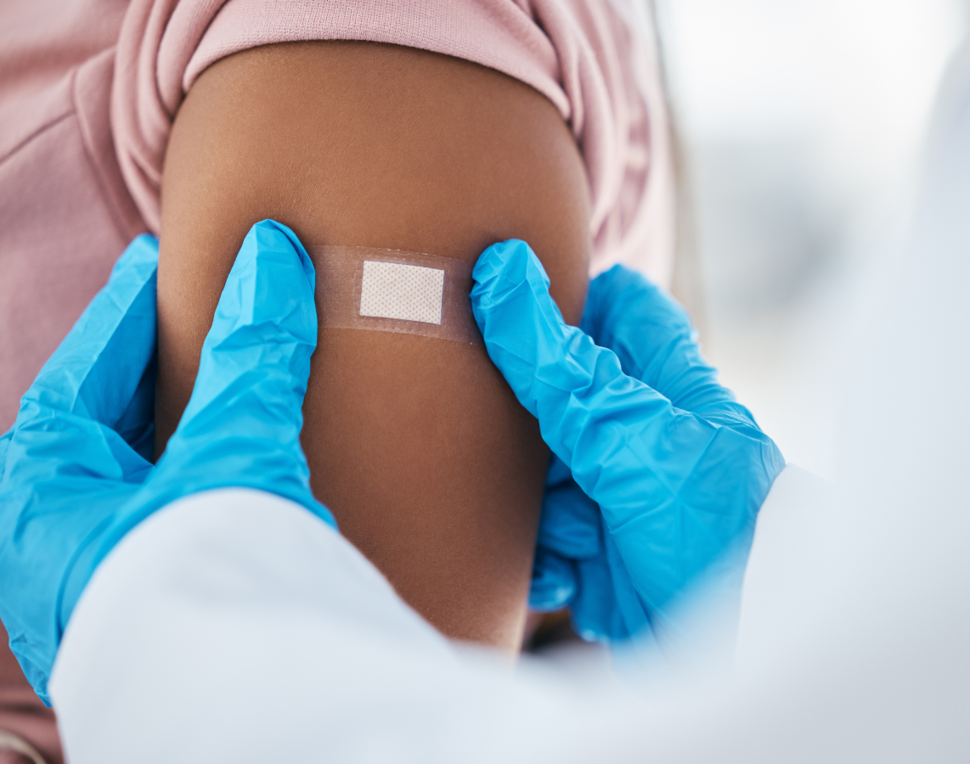 A health professional with blue gloves on presses a bandaid on a person's shoulder after vaccination.