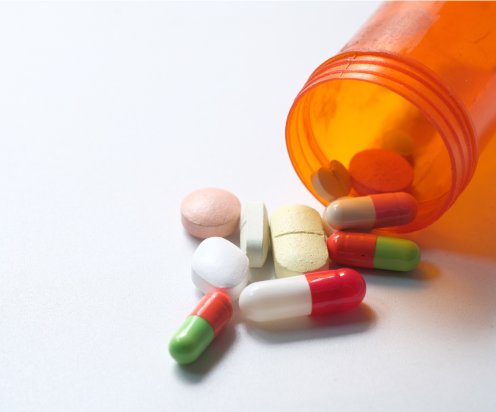 An orange prescription bottle with various pills falling out of it.