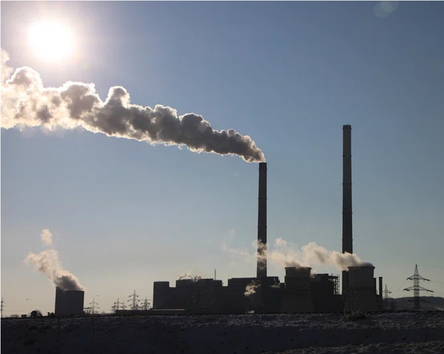 Smoke stacks emit smoke in an industrial setting on a clear, sunny day.