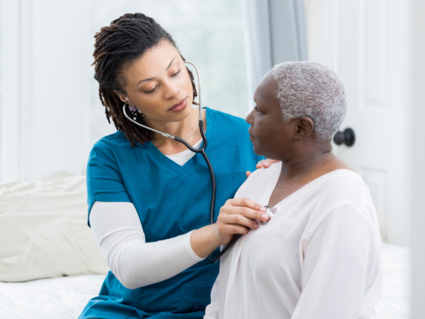 A healthcare provider checks the heart rate of a patient with a stethoscope. They are both Black women. 