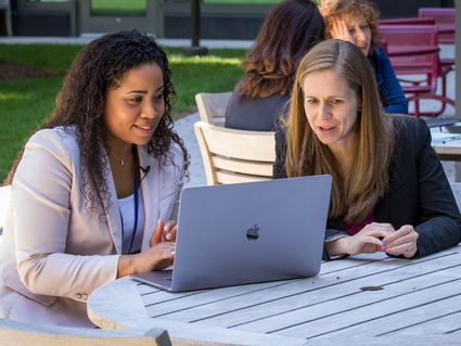 Meredith Shiels and Jennifer McGee-Avila look at data on a laptop in the terrace courtyard at the NCI Shady Grove campus. 