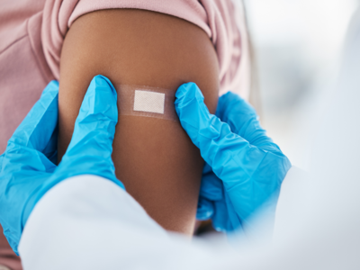 A health professional with blue gloves on presses a bandaid on a person's shoulder after vaccination.