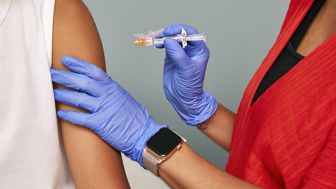 A medical professional with gloves on is administering a vaccination shot into someone's arm