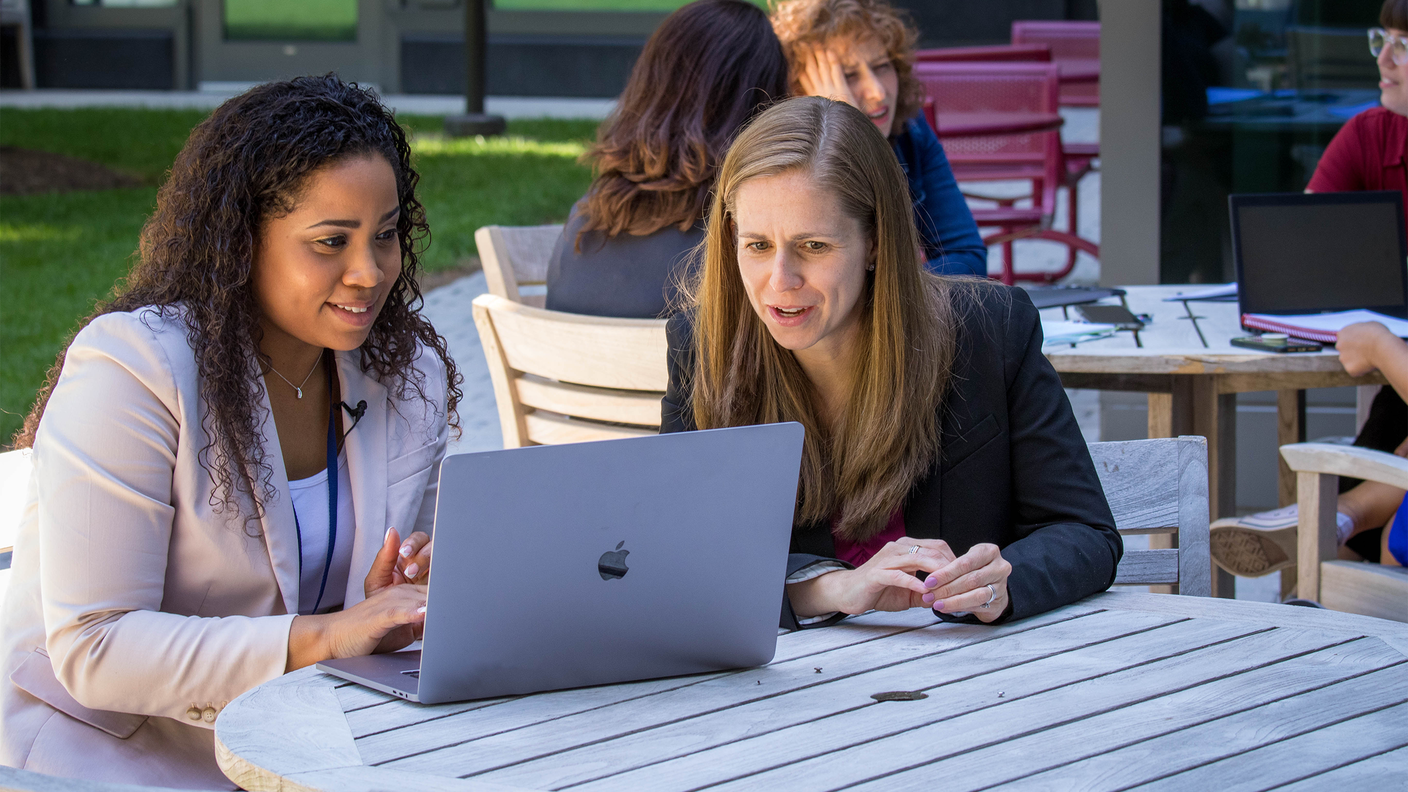 Meredith Shiels and Jennifer McGee-Avila look at data on a laptop in the terrace courtyard at the NCI Shady Grove campus. 