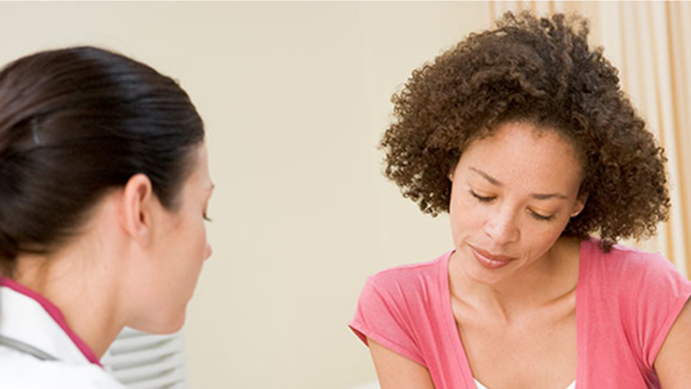 photograph of White female doctor sitting with Black female patient