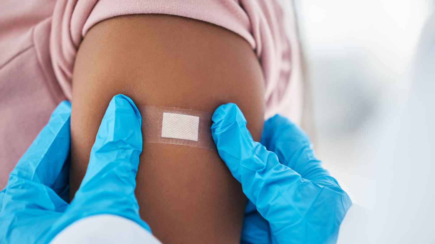 A health professional with blue gloves on presses a bandaid on a person's shoulder after vaccination.