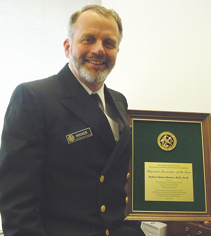 Photo of Robert Hoover clad in PHS uniform holding award plaque for the Physician Researcher of the Year.