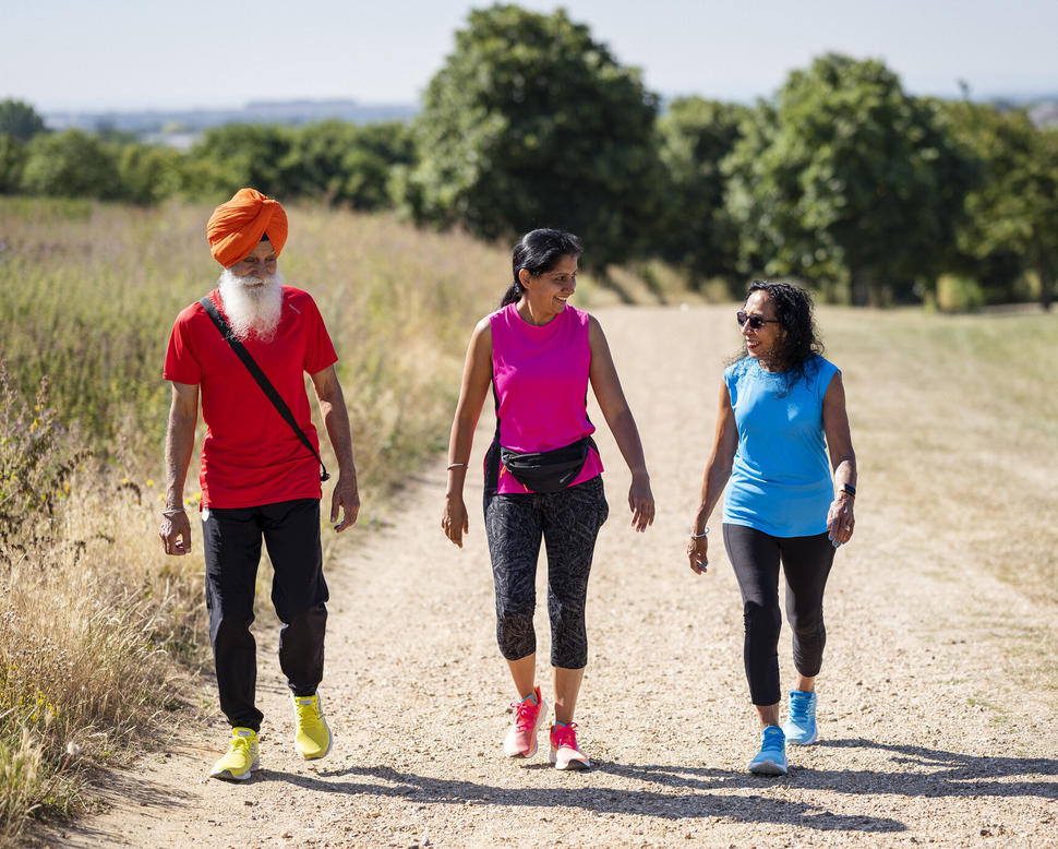 One man wearing a turban and two women walk on an outside path together.