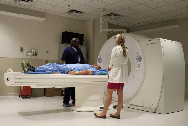 Picture of two medical professionals preparing a person for a CT scan.