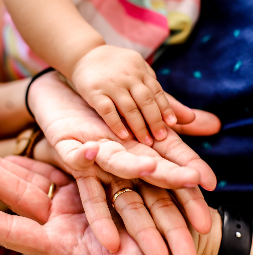 Four hands belonging to individuals of various ages stacked on top of each other, indicating the generations of a family.