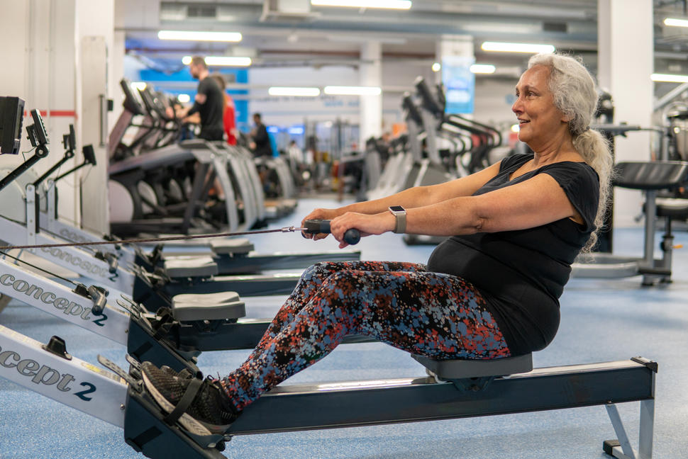 An older woman with white hair exercises on a rowing machine. 