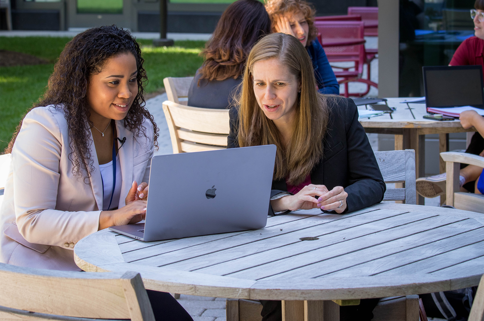 Meredith Shiels and Jennifer McGee-Avila look at data on a laptop in the terrace courtyard at the NCI Shady Grove campus. 