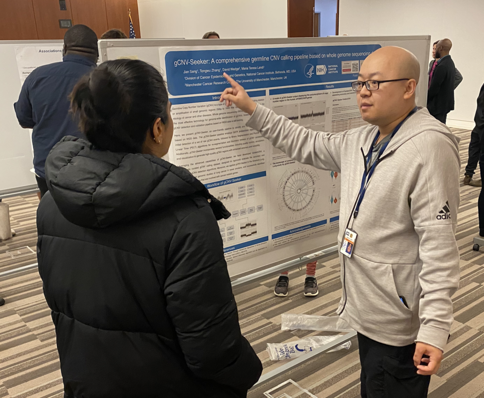 Jian Sang points to his poster as he explains his research to another person. 