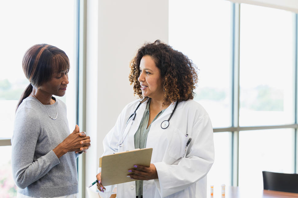 photograph of two Black women talking, a doctor and patient