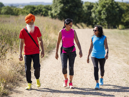 One man wearing a turban and two women walk on an outside path together.