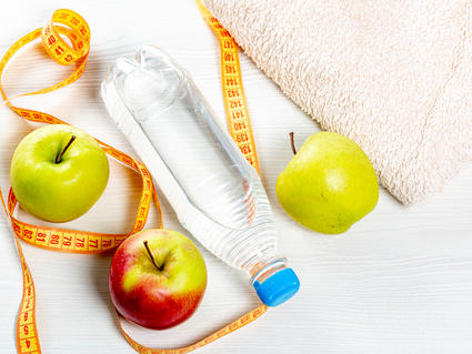 Water bottle, apples, measuring tape and towel on white wooden background. Top view