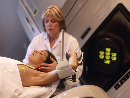A Hispanic woman (lying on her back) is being prepared for radiation therapy by a Caucasian female radiation therapist.