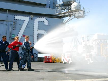 A U.S. Airmen aim a hose shooting firefighting foam. 