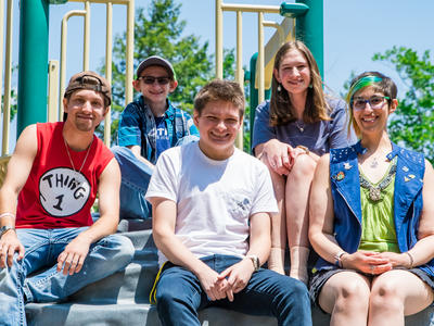 A group of adolescents with Fanconi Anemia sitting on a jungle gym and smiling. 