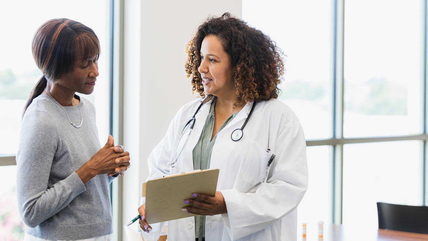photograph of two Black women talking, a doctor and patient